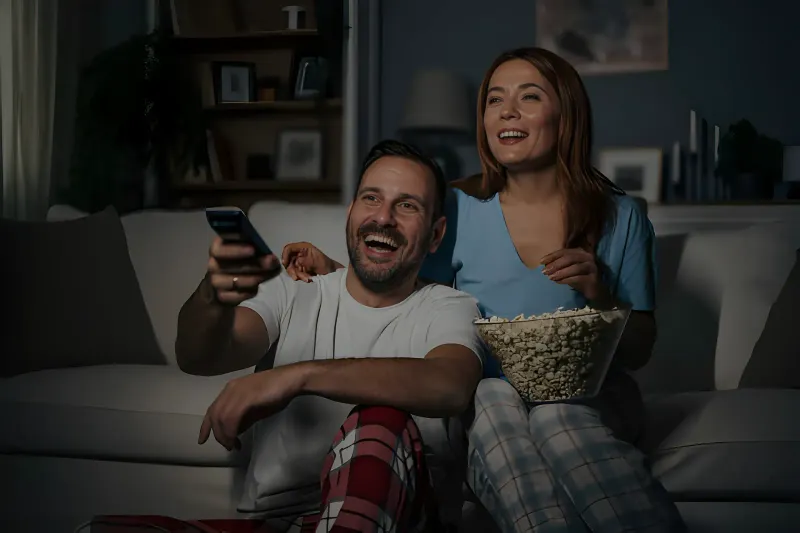 Couple relaxing on a couch at night watching Apollo Group TV IPTV with a remote and popcorn